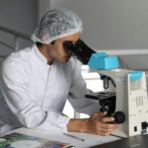 Scientist in a lab coat using a microscope to conduct research, focusing on healthcare improvements.